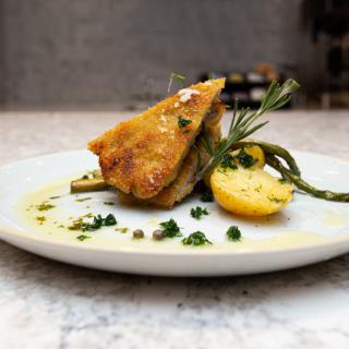 A beautifully plated gourmet dish featuring a crispy main course garnished with lemon, asparagus, and rosemary.