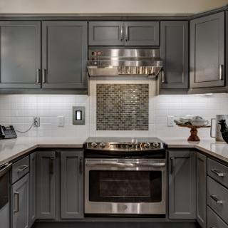 A stylish modern kitchen featuring gray cabinetry, stainless steel appliances, and a sleek white countertop.