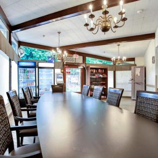 A well-lit conference room with a large table and multiple chairs, featuring chandeliers and large windows.