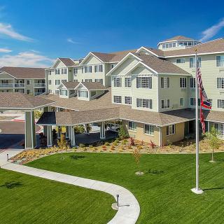 A multi-story residential building with a well-maintained lawn and flagpole under a clear blue sky.