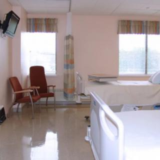 A hospital room with a bed, chairs, and a television.