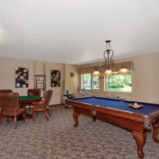 A cozy game room featuring a pool table and a poker table, with elegant lighting and wall art.