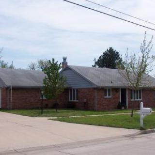 A suburban brick house with a driveway and a lawn.