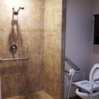 An accessible bathroom with a tiled shower and grab bars, next to a toilet equipped with support handles.