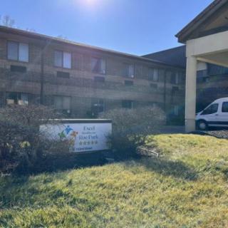 Exterior view of a hotel building with a grassy front area and a parked van.