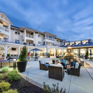 A cozy outdoor seating area in the evening, surrounded by a well-lit building and lush landscaping.