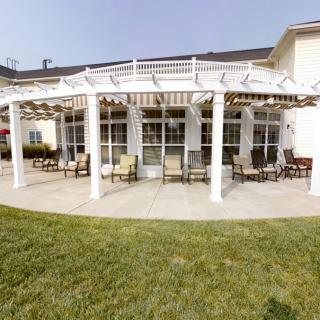 A patio area with a white pergola and outdoor seating, surrounded by a green lawn.