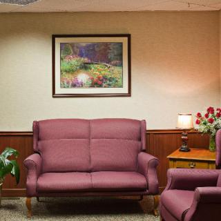 A cozy waiting room with a sofa, painting, and a table lamp.