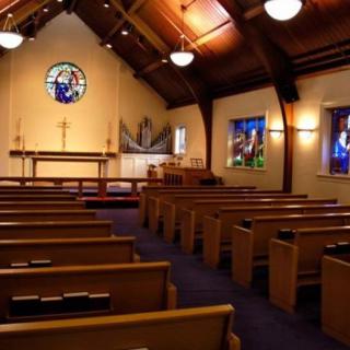 A church interior with wooden pews, stained glass windows, and an altar.