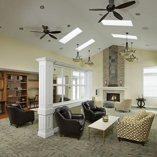 A modern living room with a cozy seating area, featuring a fireplace, ceiling fans, and skylights.