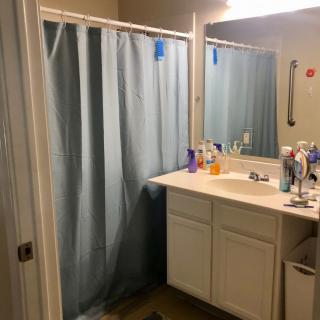 A bathroom with a shower curtain, a sink with various toiletries, and a mirror reflecting light.