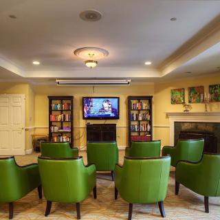 A cozy home theater setup with green chairs, a TV, bookshelves, and a fireplace.