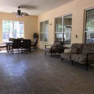 A comfortable patio area with seating arrangements, including a dining table and armchairs, complemented by large windows and a ceiling fan.