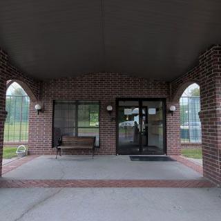 A brick building entrance with a covered area, featuring a bench and glass doors.