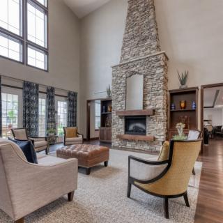Spacious living room with a stone fireplace and high ceilings, featuring elegant furniture and large windows.