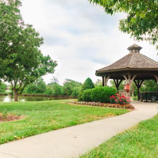 A serene view of a gazebo surrounded by lush greenery and a peaceful lake.