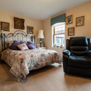 A cozy bedroom with a floral-patterned bedspread, an armchair, and various wall decorations.