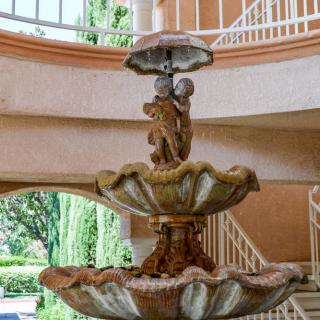 An elegant ornamental fountain in a building's interior, surrounded by staircases.