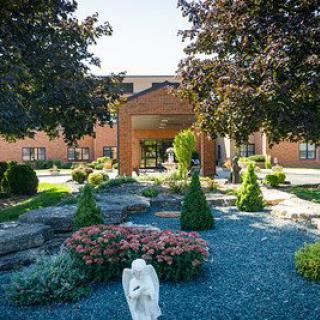 A landscaped garden with blooming flowers and trees in front of a building entrance.