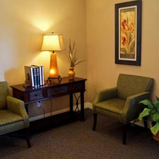 A cozy and inviting waiting area with comfortable green chairs, a warm lamp, and decorative artwork.