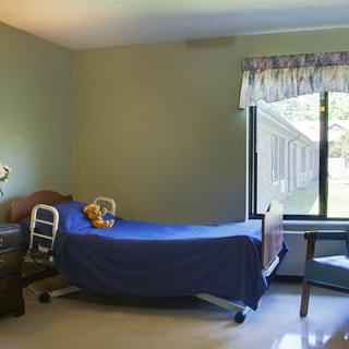 A simple hospital room with a bed, chair, and a large window allowing natural light.