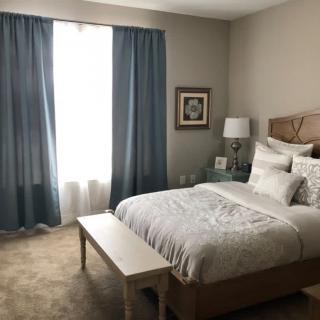 A cozy bedroom with a neatly made bed, blue curtains, and warm lighting.