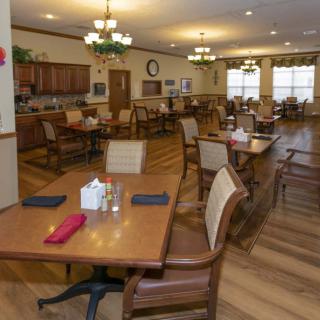 A cozy dining room with neatly arranged tables and chairs, featuring warm lighting and wood flooring.