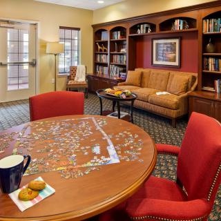 A cozy library room with bookshelves, a puzzle on the table, and comfortable seating.