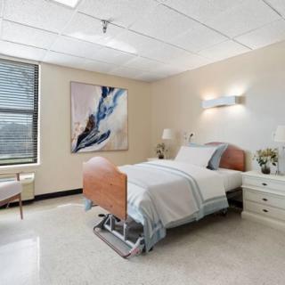 A modern hospital room with a single bed, nightstand, and large window providing natural light.
