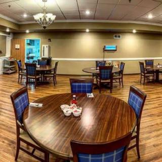 A cozy dining room with wooden tables and blue cushioned chairs, featuring warm lighting and a spacious layout.