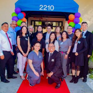A group of people gathered for an event, standing on a red carpet with colorful balloons in the background.