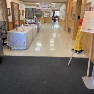 A spacious hallway in an office building, featuring tables on the sides and a cleaning sign.