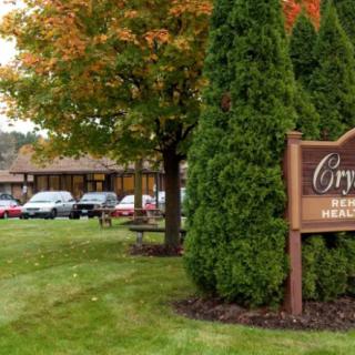 A motel with a wooden sign, surrounded by trees and a parking area with cars.
