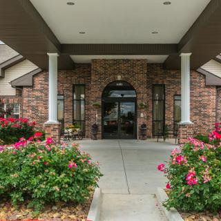 A brick building entrance with blooming flowers and columns.
