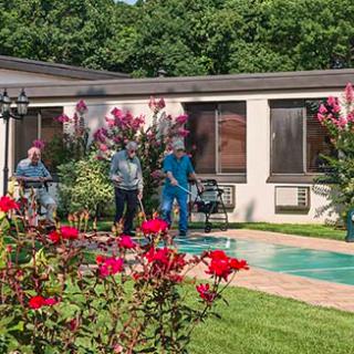 A group of people standing near a pool surrounded by red flowers and greenery.