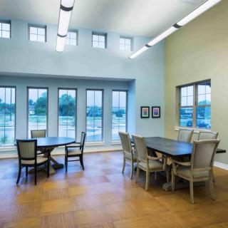 A modern dining area with tables and chairs, well-lit by natural daylight through large windows.