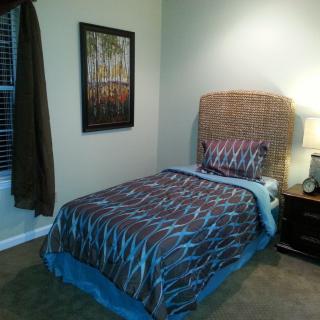 A cozy bedroom with a single bed, adorned with patterned bedding and a bedside lamp.