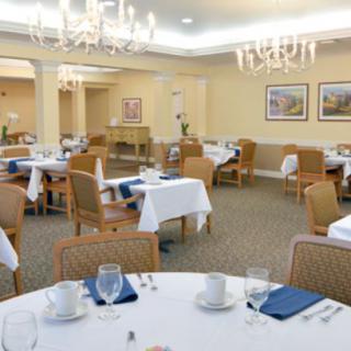 A well-appointed dining room with neatly arranged tables and chairs, illuminated by elegant chandeliers.