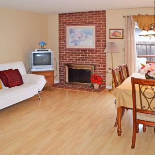 A cozy living room featuring a brick fireplace, wooden flooring, a sofa, and a dining table.