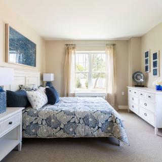 A well-decorated bedroom with a large bed, two side tables, and a chest of drawers, illuminated by natural light from a window.