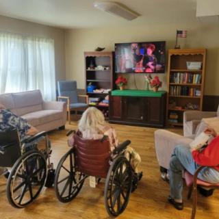 Elderly individuals in wheelchairs watching television in a nursing home living room.