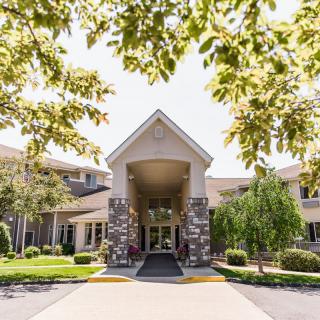 A view of a building entrance surrounded by trees and landscaping on a sunny day.