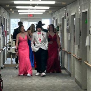 A group of students in formal attire walking down a hallway, possibly attending a prom or similar event.
