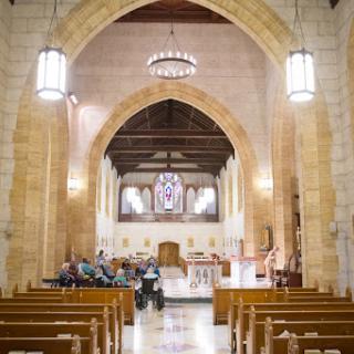 A serene view of the interior of a gothic-style church, featuring wooden benches and elegant lighting.