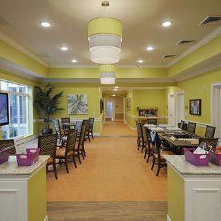 A spacious dining room with yellow walls, set with tables and chairs, featuring decorative lighting.