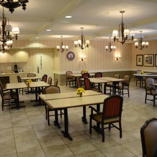 An empty dining room with neatly arranged tables and chairs, illuminated by chandeliers.