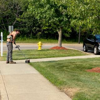 A man uses a string trimmer to tidy up the edges of a sidewalk in a well-maintained yard.
