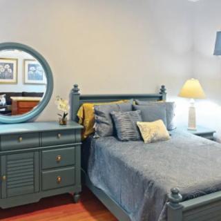 A cozy bedroom featuring a bed with blue bedding, a matching dresser with a round mirror, and a bedside lamp.