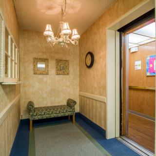 A neatly decorated hallway with an open elevator, a bench, and a chandelier.
