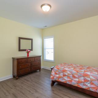 A minimalist bedroom with a wooden dresser, mirror, and single bed featuring a colorful bedspread.